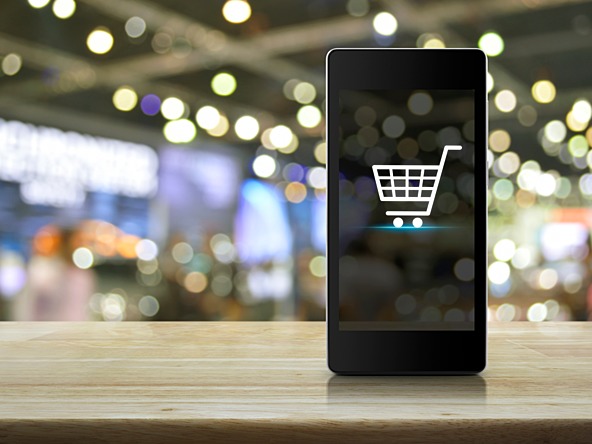 Smartphone propped up against a blurred shopping background with a picture of a shopping basket on its screen